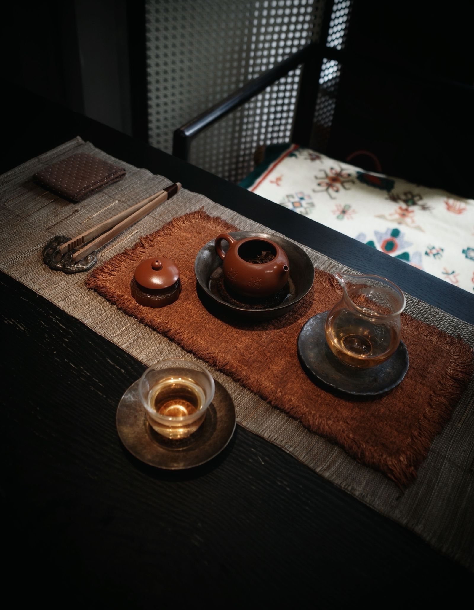A dark traditional Chinese tea setting with a clay teapot and clear vessels holding amber tea.